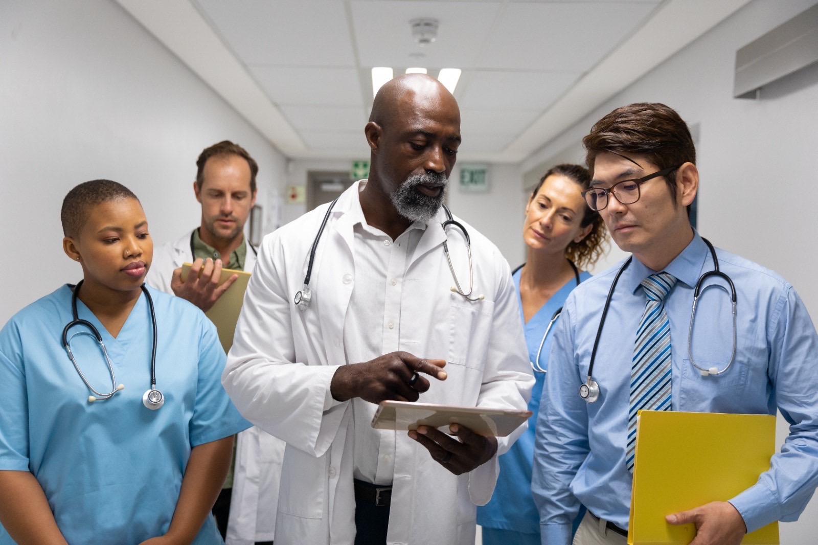 diverse group male female doctors walking through corridor looking tablet